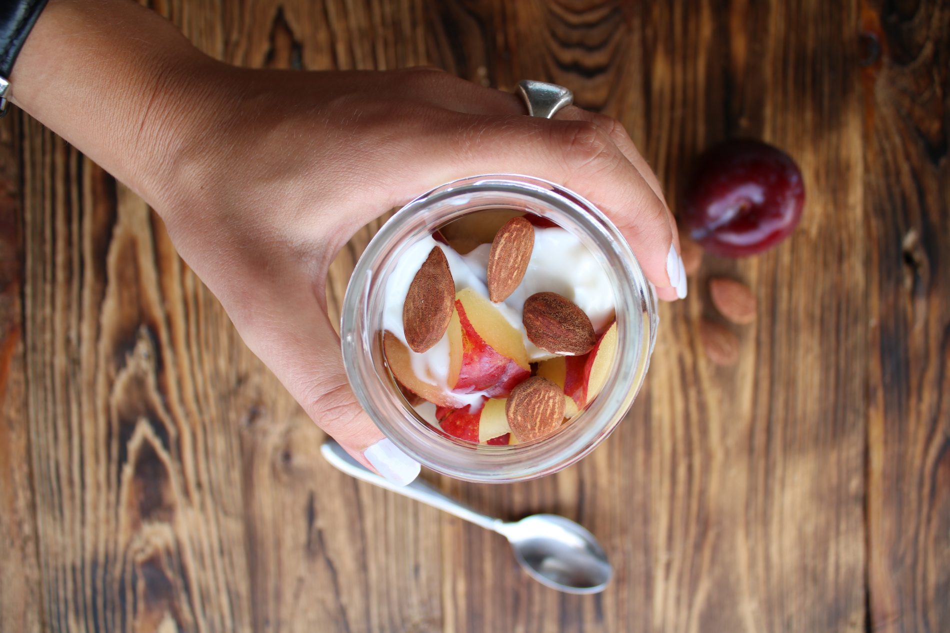 mano di una donna che prende sul tavolo di legno uno yogurt con prugna e mandorle