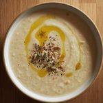 Minestra di semolino: un primo piatto cremoso pronto in 5 minuti 1 In primo piano su un tavolo di legno chiaro, una calda minestra di semolino condita con dell'olio, qualche erba aromatica e della frutta secca.