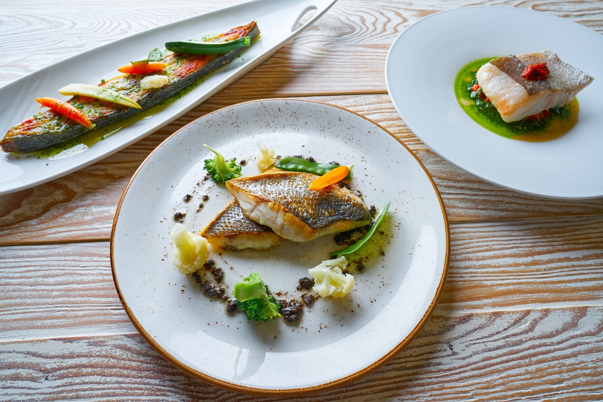 su tavolo di legno: 3 piatti bianchi con ricette con il rombo e verdure