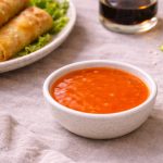 in primo piano ciotola con salsa agrodolce cinese e sullo sfondo piatto di involti primavera