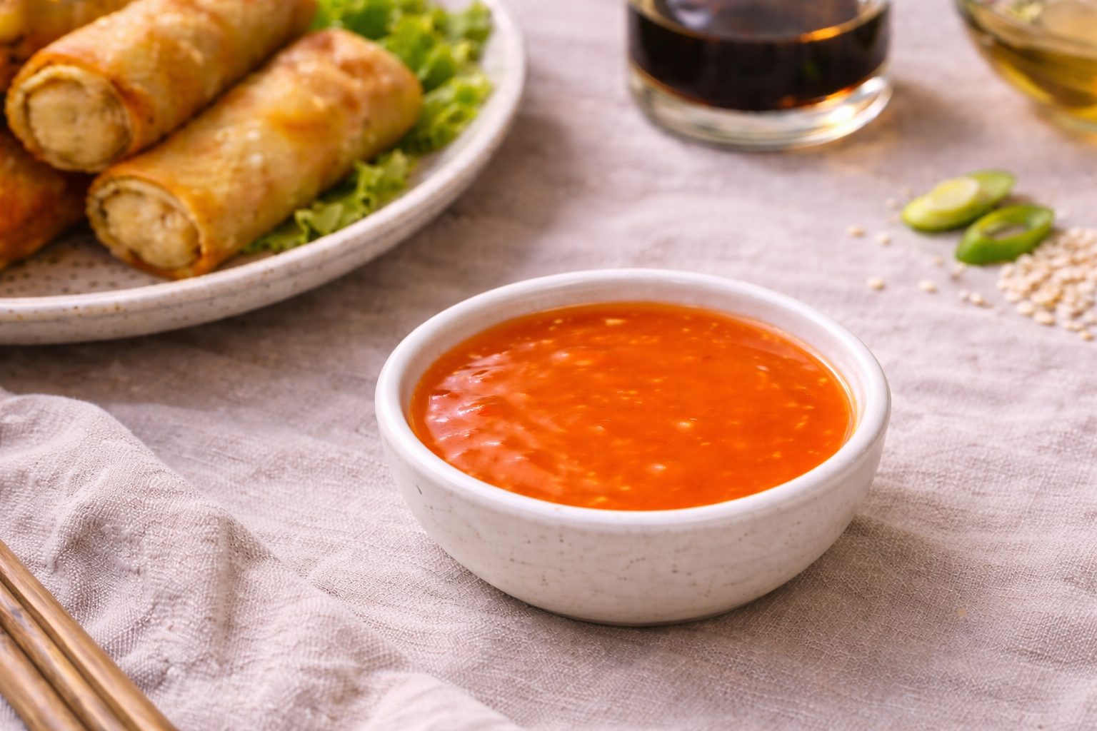 in primo piano ciotola con salsa agrodolce cinese e sullo sfondo piatto di involti primavera