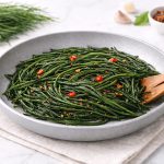 In primo piano su uno sfondo chiaro, ci sono degli agretti in padella conditi con del peperoncino.