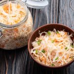 su tavolo di legno barratolo di vetro con verdure fermentate e accanto ciottola di legno con 1 porzione di verdure