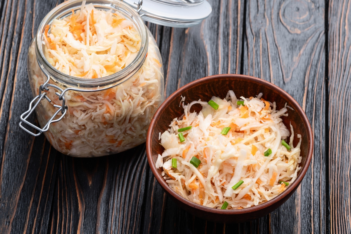 su tavolo di legno barratolo di vetro con verdure fermentate e accanto ciottola di legno con 1 porzione di verdure
