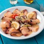 Carpaccio di pesce spada marinato agli agrumi 1 In primo piano su un tavolo azzurro di legno, c'รจ un piatto di carpaccio di pesce spada condito con delle fettine di limone.