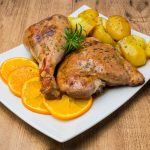 su piatto bianco due pezzi di tacchino al forno con patate e fette di arancia