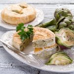 primo piano sul tavolo di una torta con carciofi tagliata con accanto i carciofi