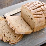 Pane senza glutine: ricetta fatta in casa facile e soffice 1 primo piano di un tagliere di legno con il coltello con un pane senza glutine tagliato a fette