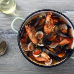 Zuppa di cozze alla napoletana: ricetta originale passo passo 1 In primo piano su un tavolo da cucina grigio c'รจ una pentola con la zuppa di cozze alla napoletana. Sulla sinistra delle posate e un piatto fondo giallo.