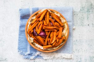 Iscriviti subito alla dieta Melarossa e scarica l'app 12 Carote in friggitrice ad aria speziate servite in una ciotola di terracotta, su carta forno e tovagliolo azzurro.