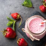 Frullato di fragole: ricetta facile, fresca e leggera 1 su sfondo cucina di marmo, vista dall'alto, un bicchiere da frullato con un frullato di fragole e una cannuccia bianca e rossa con attorno fragole