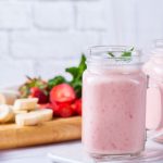 Frullato di frutta fatto in casa: ricetta e varianti 1 in cucina su tagliere banane e fragole lavate e tagliate a fette, davanti 2 bicchieri grandi pieni di frullato di frutta