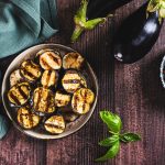 Melanzane in friggitrice ad aria: ricetta facile, leggera e croccante 1 su tavolo di legno ciotola con melanzane in friggitrice ad aria. Accanto tovagliolo verde e sulla destra 2 melanzane e in un altra ciotola pepe nero