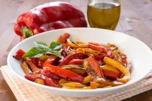 Iscriviti subito alla dieta Melarossa e scarica l'app 14 su tavolo piatto bianco sotto un canovaccio giallo e bianco con peperoni in friggitrice ad aria. Accanto una bottiglia di olio EVO e un peperone rosso intero