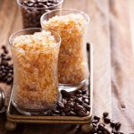 Granita al caffè: ricetta facile senza gelatiera 1 Due bicchieri di granita al caffè serviti su un vassoio con chicchi di caffè e un cucchiaino.