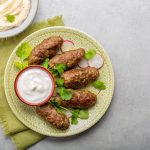 Kofta alla piastra: polpette speziate facili e veloci 1 In primo piano su un piatto con delle decorazioni in verde ci sono delle kofta con una salsa allo yogurt.