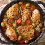 Pollo in padella alla mediterranea: ricetta tenera con pomodorini e olive 1 In primo piano su un tavolo di legno c'è una casseruola con del pollo in padella alla mediterranea pomodorini e olive.