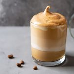 Spumone al caffè: la ricetta facile e veloce senza panna 1 Spumone al caffè servito in un bicchiere di vetro, con spuma soffice in superficie e chicchi di caffè accanto.