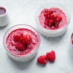 Coulis di lamponi: ricetta facile senza zucchero 1 In primo piano su uno sfondo chiaro ci sono delle coppette di vetro con delle cheesecake e coulis di lamponi. Sulla destra c'รจ una ciotola con dei lamponi freschi, mentre sullo sfondo la coulis di lamponi dentro un bricchetto bianco.