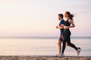 Iscriviti subito alla dieta Melarossa e scarica l'app 10 sulla spiaggia un uomo e una donna corrono assieme felici perché conoscono i benefici della corsa