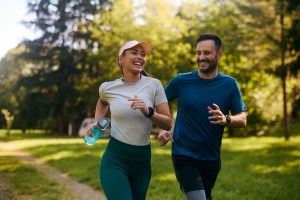 Home Page 67 un uomo e donna sorridenti corrono all'alba al parco. Stanno praticando una seduta di fartlek, la donna ha leggings e un capello e tiene in mano una borraccia