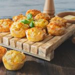 Muffin salati: ricetta base soffice e veloce 1 In primo piano su un tagliere in legno ci sono dei muffin salati soffici e dorati.