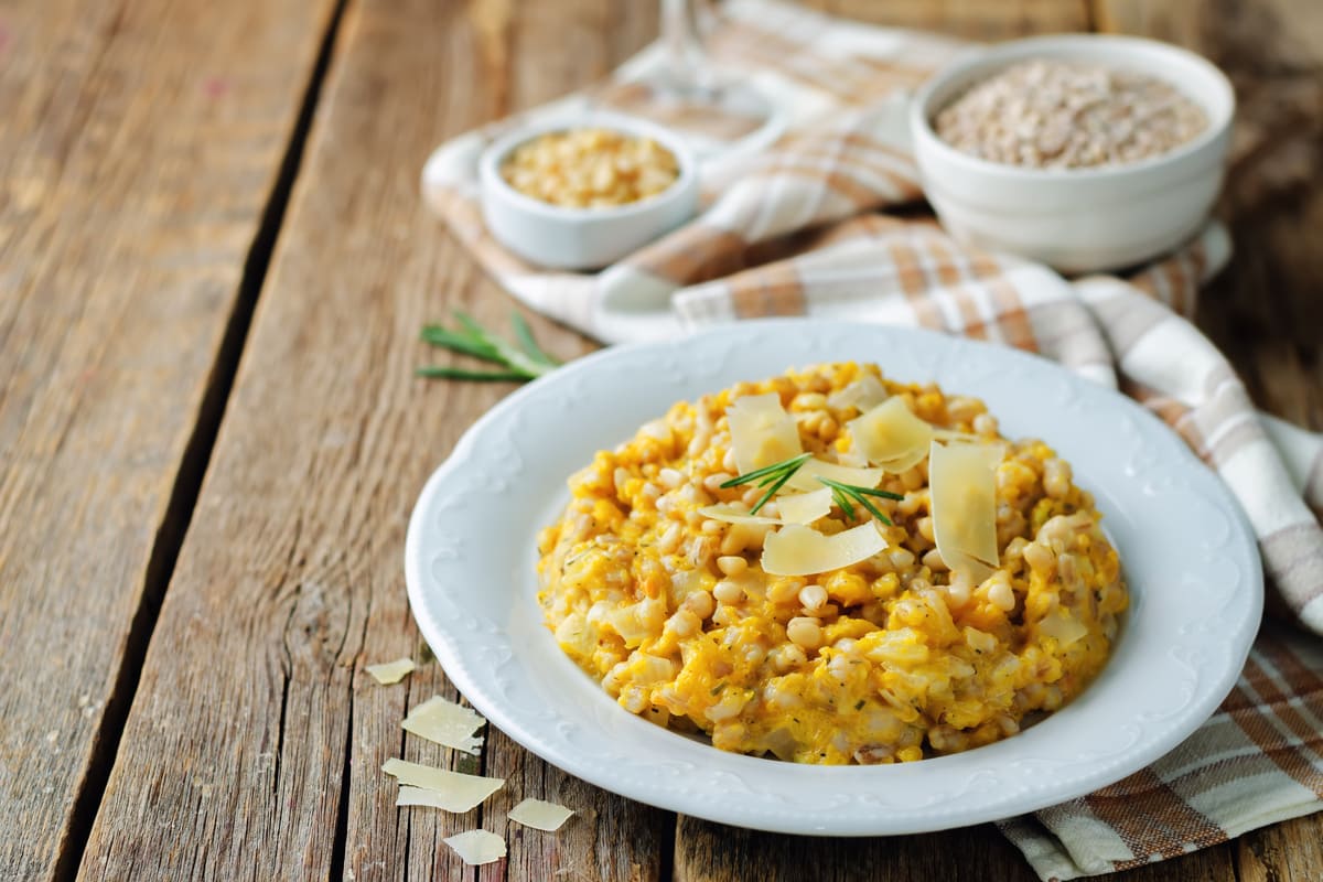 Orzotto alla zucca con scaglie di Parmigiano e rosmarino servito in un piatto bianco.