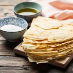 Pane guttiau, la ricetta sarda croccante e fragrante 1 In primo piano su un tavolo di legno c'è del pane guttiau con del sale e dell'olio extra vergine d'oliva.
