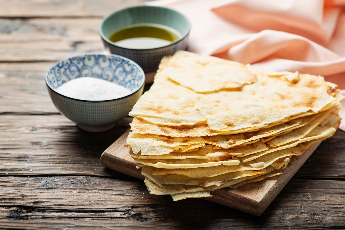 Pane: dalla pizza alle polpette, 11 idee per usarlo come ingrediente in cucina 11 In primo piano su un tavolo di legno c'è del pane guttiau con del sale e dell'olio extra vergine d'oliva.