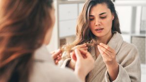 Iscriviti subito alla dieta Melarossa e scarica l'app 10 donna davanti allo specchio controlla i capelli caduti che tiene tra le mani