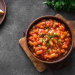 Fagioli alla messicana: ricetta facile, saporita con video 1 In primo piano su un tagliere in legno ci sono dei fagioli alla messicana conditi con del prezzemolo fresco. Sullo sfondo delle fette di pane tostato.