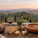 Fagioli al Rosso di Montepulciano: la ricetta dei fagioli ubriachi 1 Fagioli al vino rosso in ciotola di terracotta con pane, vino, aglio e rosmarino su un tavolo rustico affacciato sulle colline toscane.