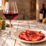 Mele cotogne al vino rosso: ricetta facile e profumata 1 su tavolo di legno, sulla sinistra mele cotogne, al centro piatto bianco con mele cotogne al vino rosso, dietro un calice di vino e dietro bottiglie di vino rosso