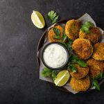 Polpettine di fagioli al forno facili e sfiziose 1 In primo piano su uno sfondo scuro ci sono delle polpettine di fagioli con una salsa allo yogurt e degli spicchi di limone.