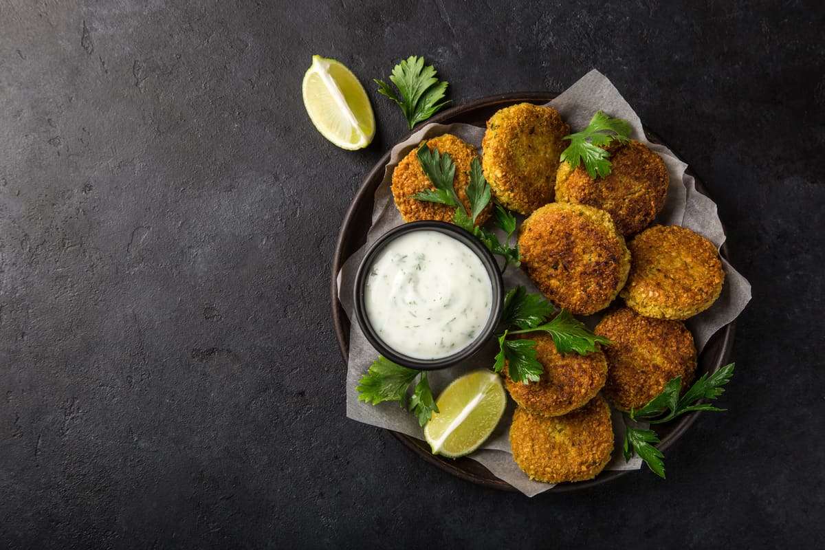 In primo piano su uno sfondo scuro ci sono delle polpettine di fagioli con una salsa allo yogurt e degli spicchi di limone.