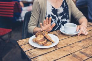 Iscriviti subito alla dieta Melarossa e scarica l'app 14 donna seduta a un tavolo di legno rifiuta con la mano un piatto con delle fette biscottate